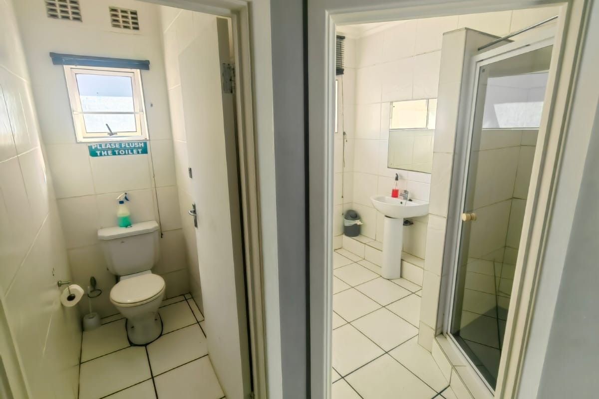A functional commercial bathroom suite featuring a separate toilet cubicle and a shower area with a pedestal basin.