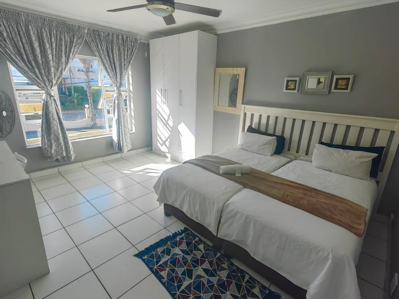 A well-lit bedroom featuring tiled flooring, a ceiling fan, and a built-in wardrobe, offering a clean and functional space.