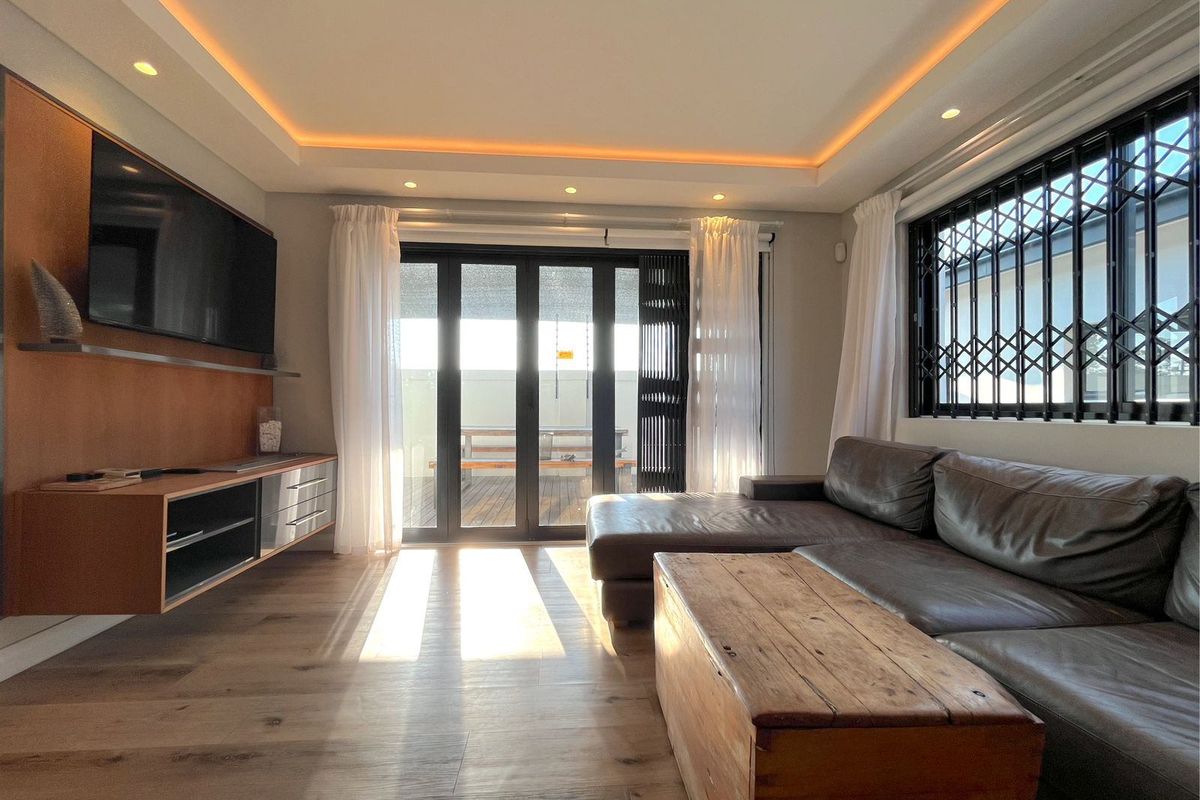 Modern living room featuring recessed tray ceiling with ambient lighting, wood-look flooring, and large sliding glass doors leading to an outdoor patio area.