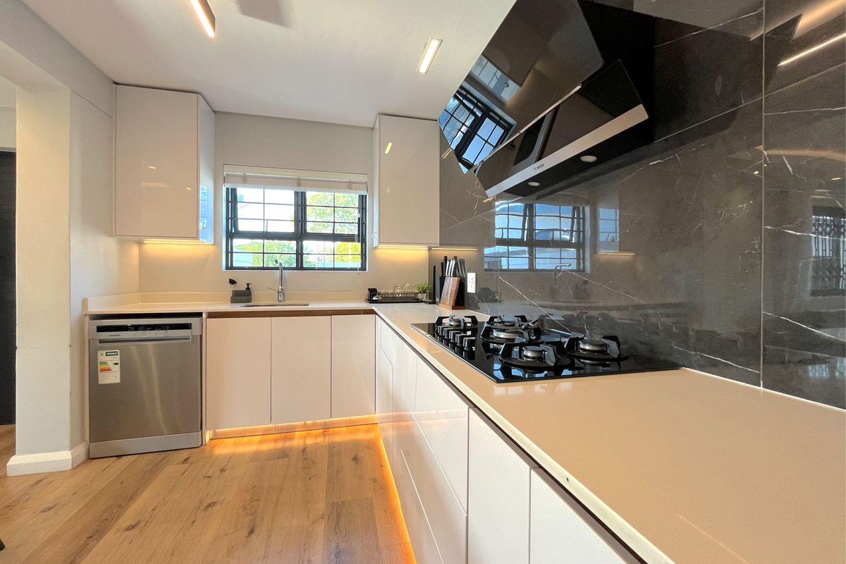 Modern kitchen featuring sleek white cabinetry, stone countertops, a gas hob with extractor fan, and integrated lighting, complemented by wood-look flooring.