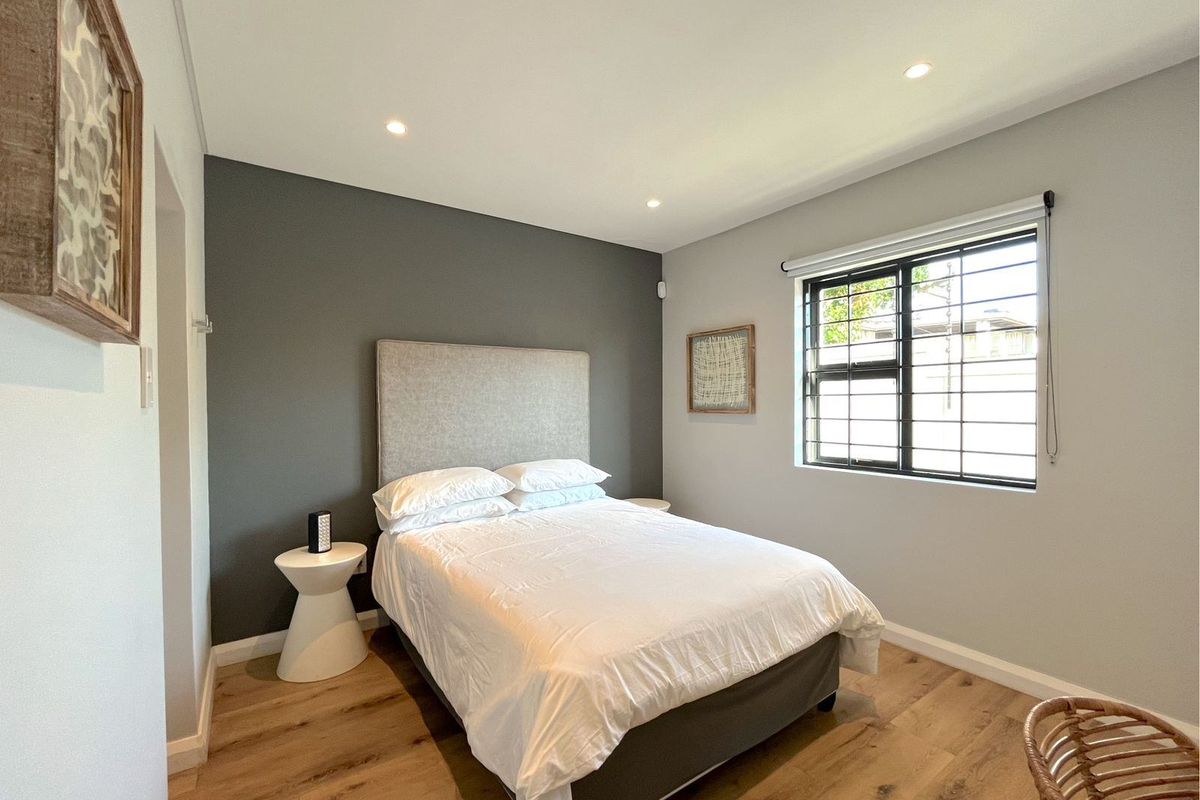A well-maintained bedroom featuring modern wood-look flooring, a dark grey feature wall, recessed downlighting, and a window with security bars.