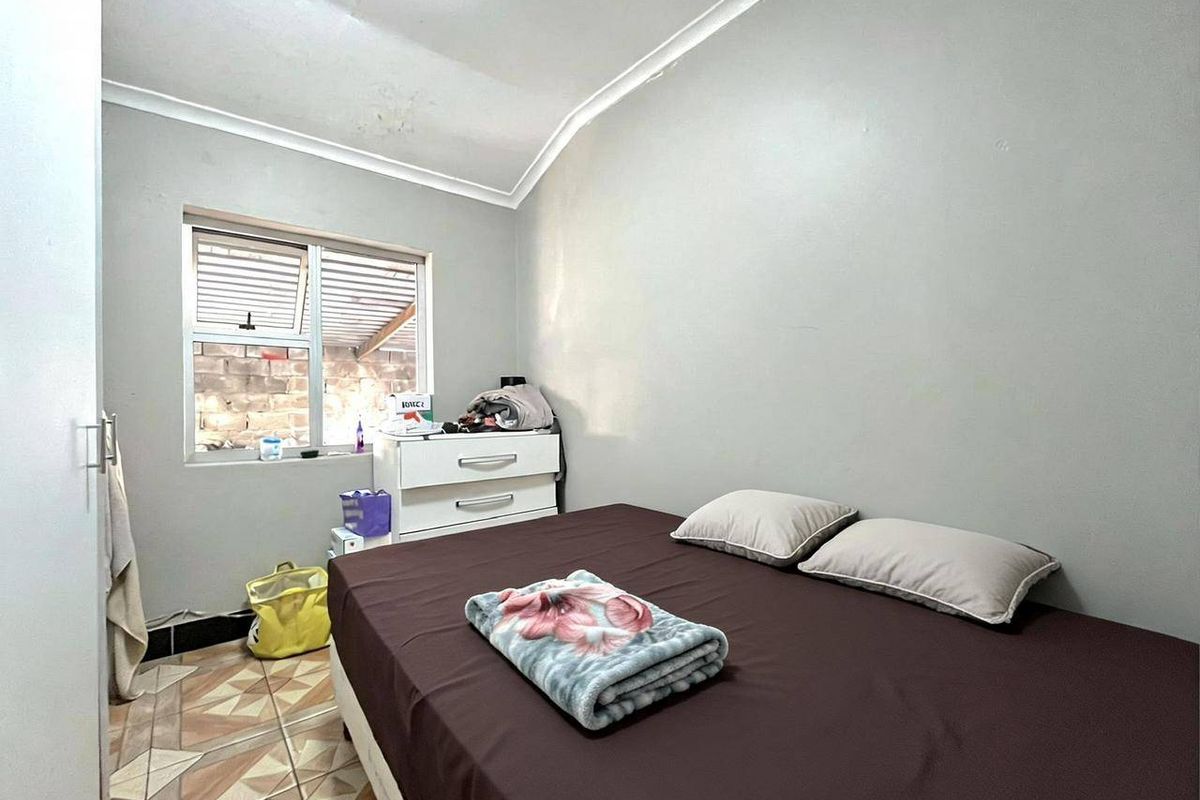 A compact bedroom featuring tiled flooring, a window with security bars, and coved ceiling detailing.