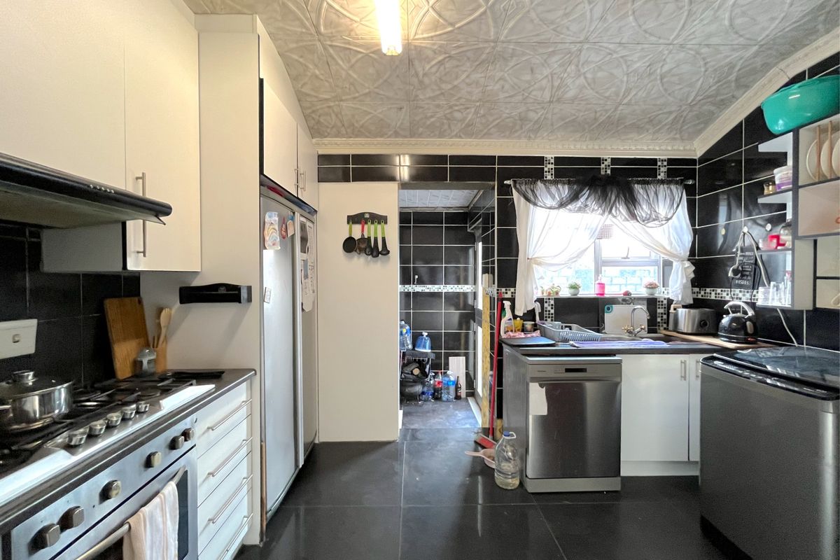 A functional kitchen featuring black tiled walls, white cabinetry, a gas stove, and a textured ceiling, with an adjacent scullery area.
