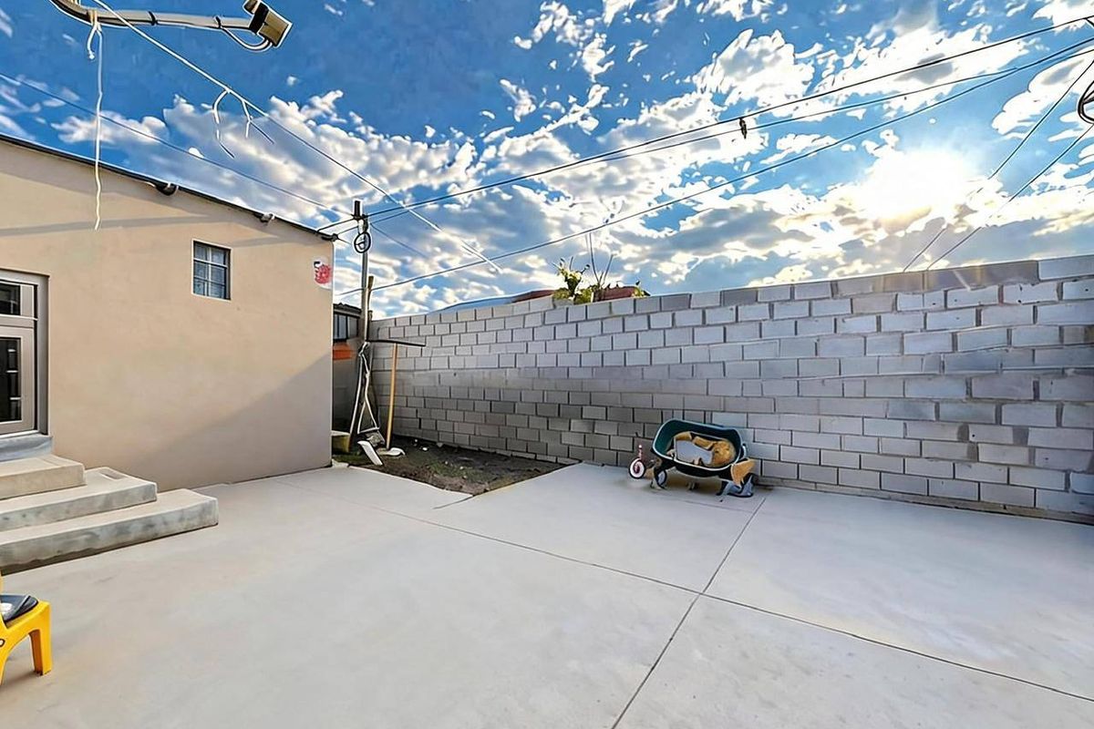A rear exterior view featuring a concrete patio area, a plain rendered building facade, and a high concrete block boundary wall.