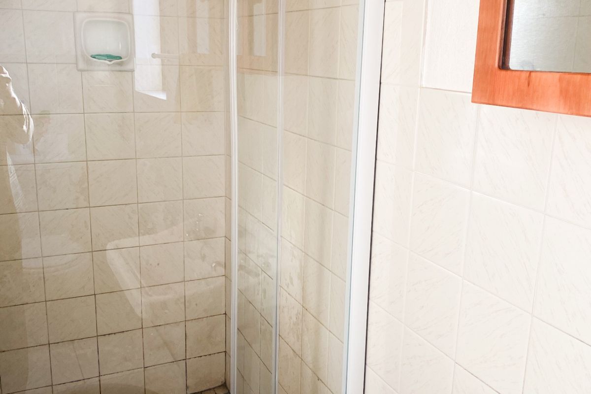 A functional bathroom featuring a glass-enclosed shower with tiled flooring and a wall-mounted basin.