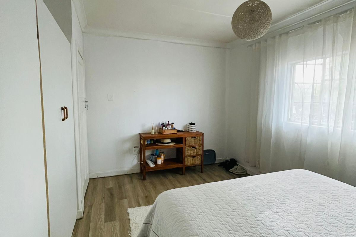 A bright bedroom featuring light wood-look flooring, built-in wardrobe cabinetry, and a large window allowing for natural light.