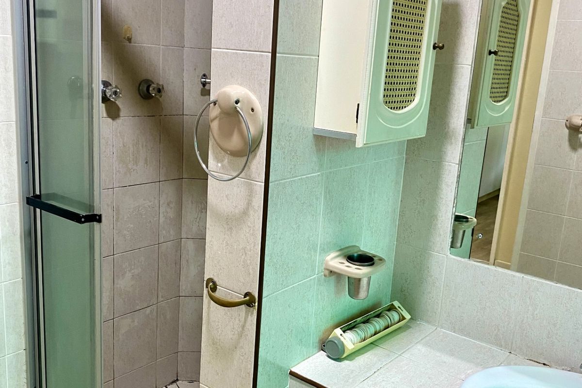 A dated bathroom featuring a tiled shower enclosure with a glass door, a built-in vanity with a basin, and wall-mounted storage cabinetry.