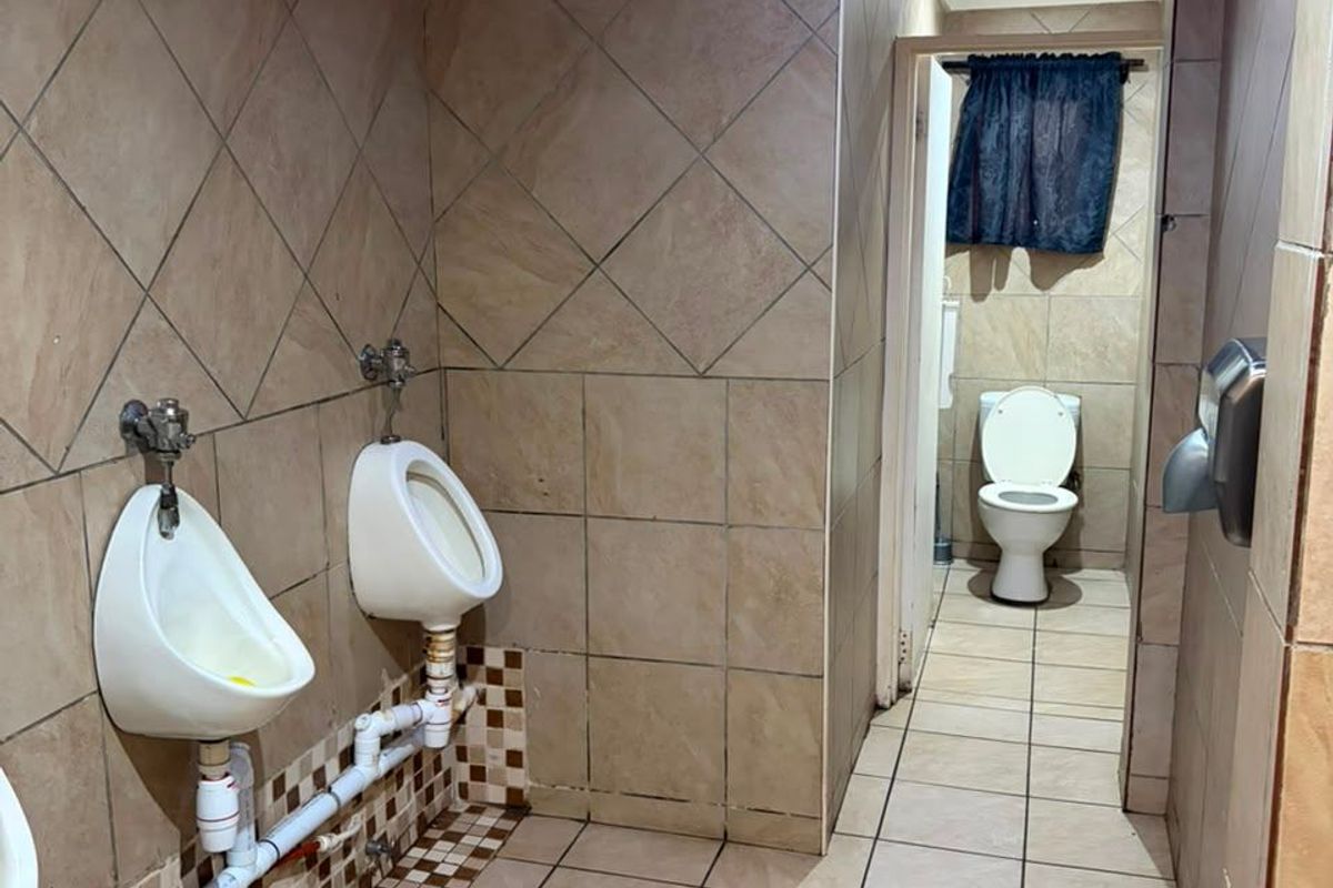 Commercial restroom facility featuring wall-mounted urinals with exposed plumbing and a separate toilet cubicle with tiled finishes throughout.