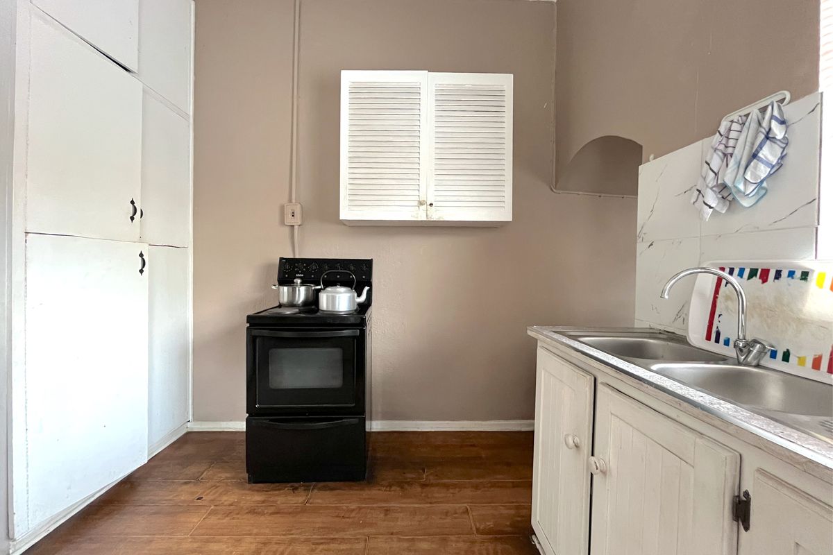A functional kitchen area featuring built-in white cabinetry, a double stainless steel sink, and a freestanding stove with wall-mounted storage.