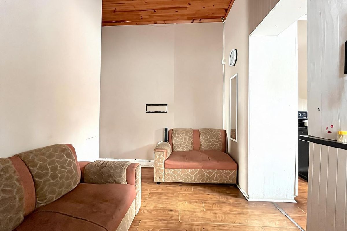 A living area featuring wood-look flooring and a timber-paneled ceiling, with an open-plan layout leading into the adjacent kitchen space.