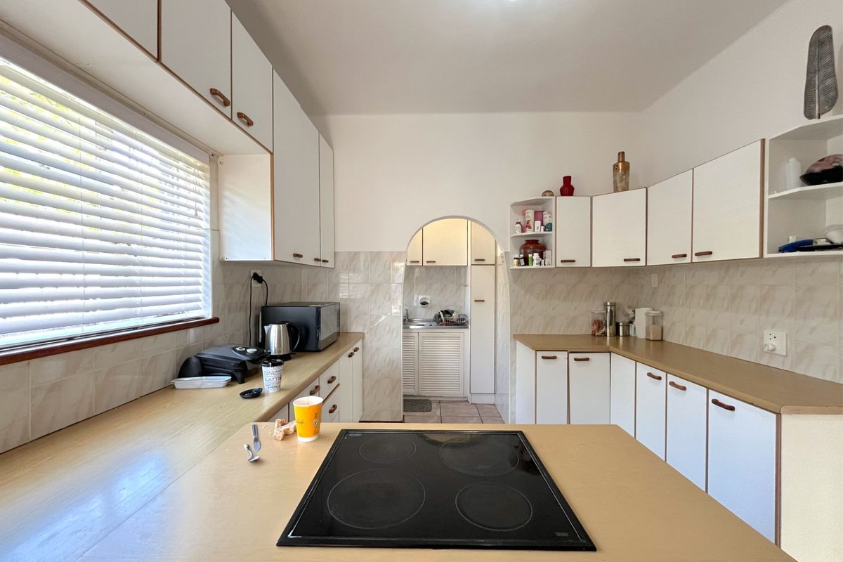 A functional kitchen featuring laminate countertops, built-in cabinetry, and a central electric hob, with an adjoining scullery area visible through the arched doorway.