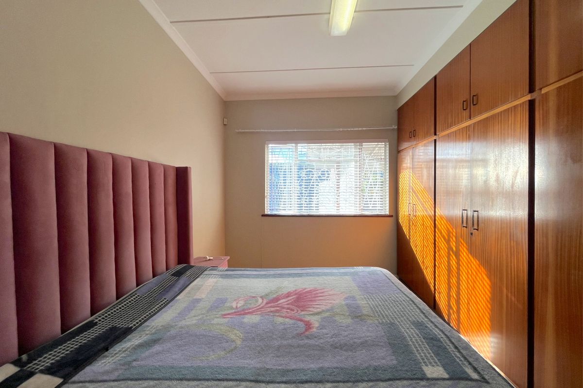 A bedroom featuring built-in wooden cupboards, a window with blinds, and a standard ceiling light fixture.