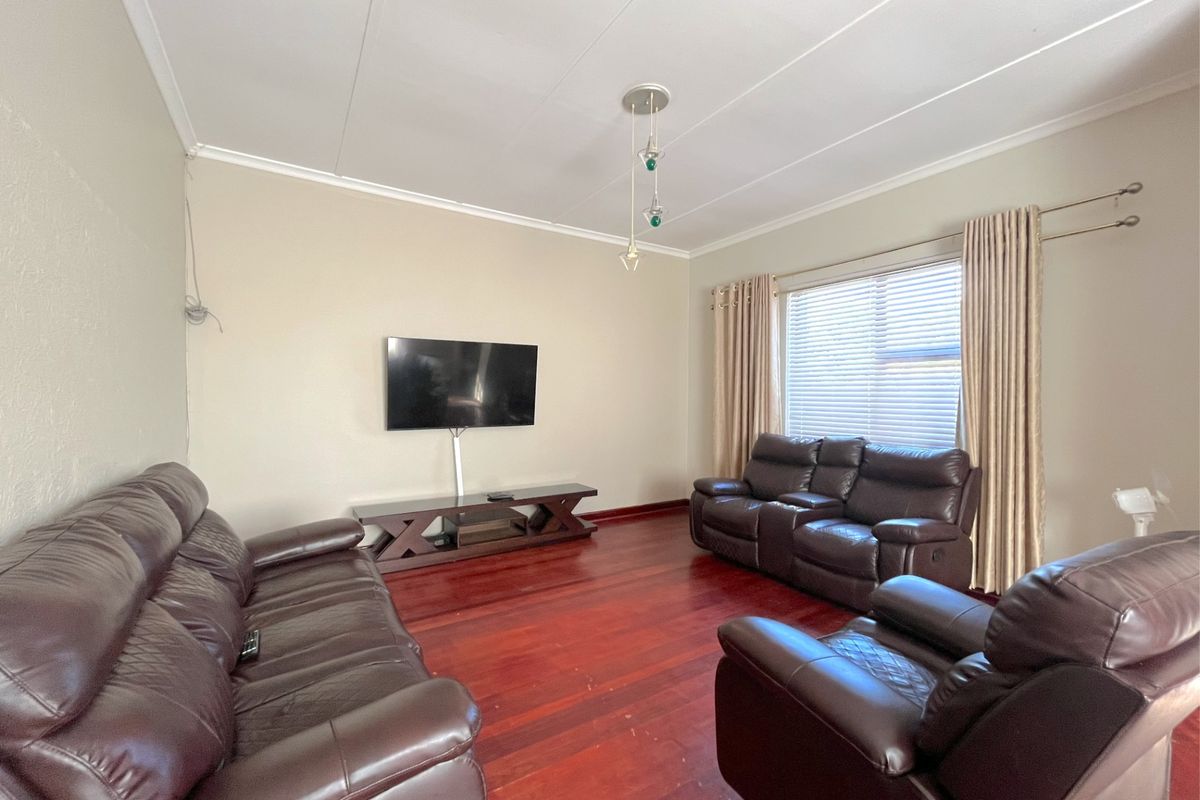 A living room featuring polished hardwood flooring, a large window with fitted curtains, and a wall-mounted television.