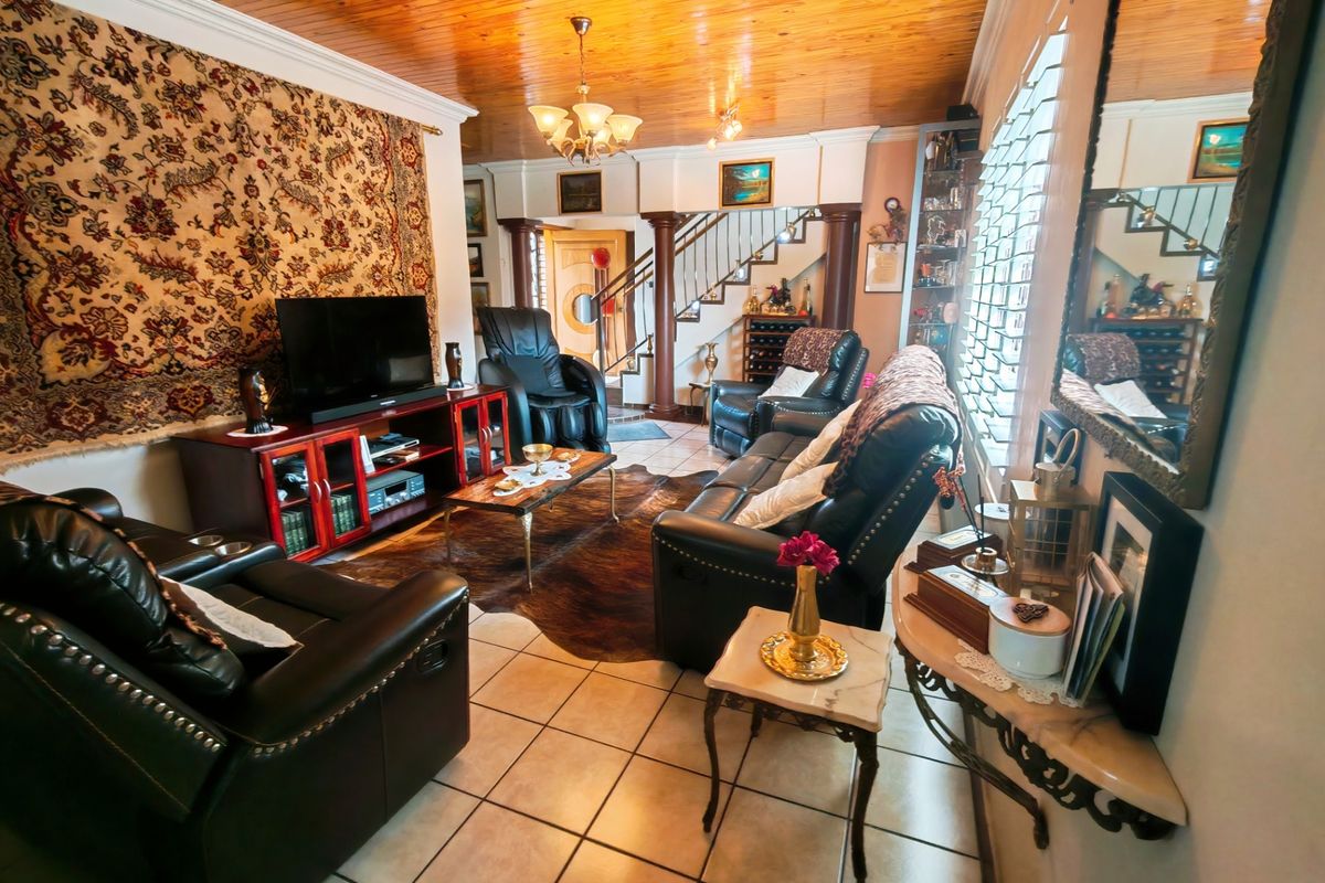 A living room featuring a timber-clad ceiling, tiled flooring, and a staircase with decorative columns, offering a traditional aesthetic.