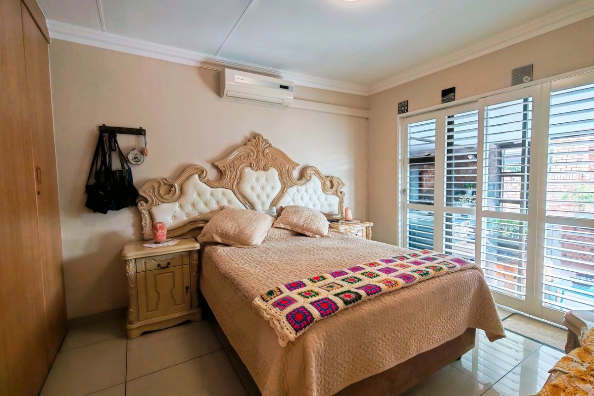 A well-maintained bedroom featuring tiled floors, built-in cupboards, a split-system air conditioner, and sliding glass doors with plantation shutters leading to the exterior.