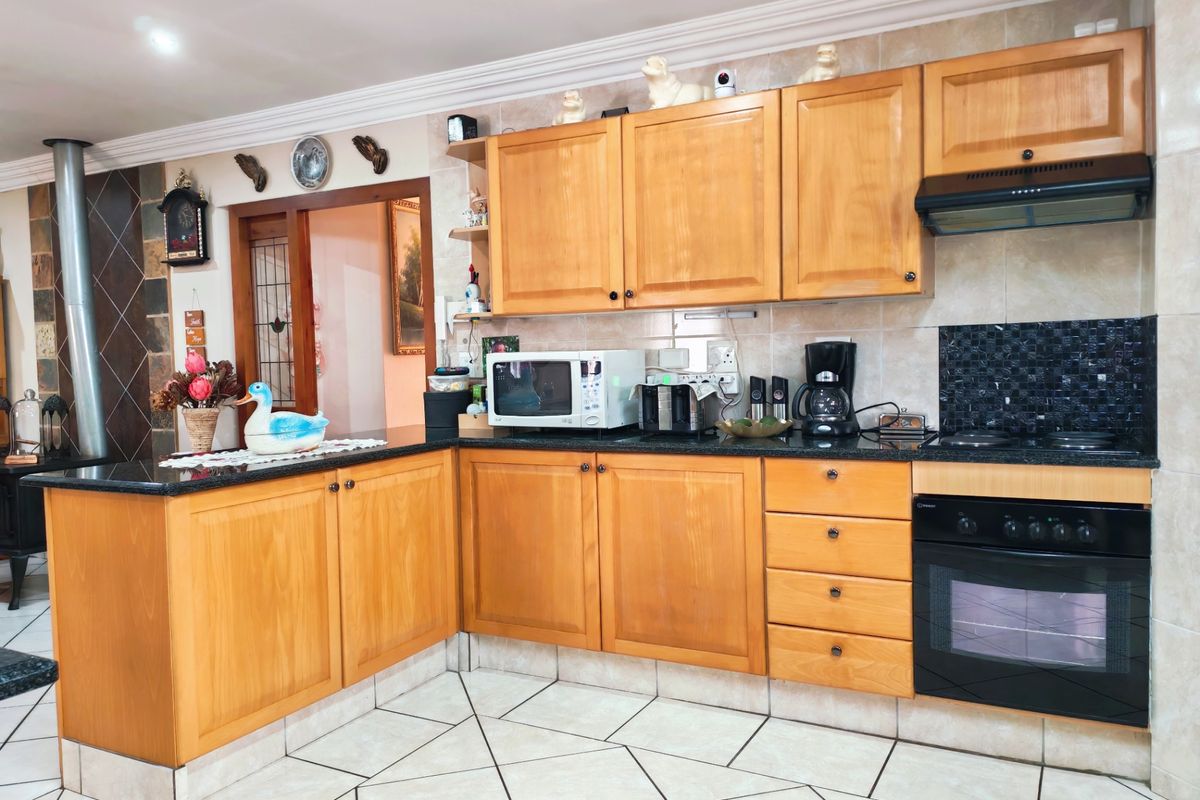 A functional kitchen featuring wooden cabinetry, granite countertops, built-in oven, hob, and extractor fan, complemented by tiled flooring and backsplash.