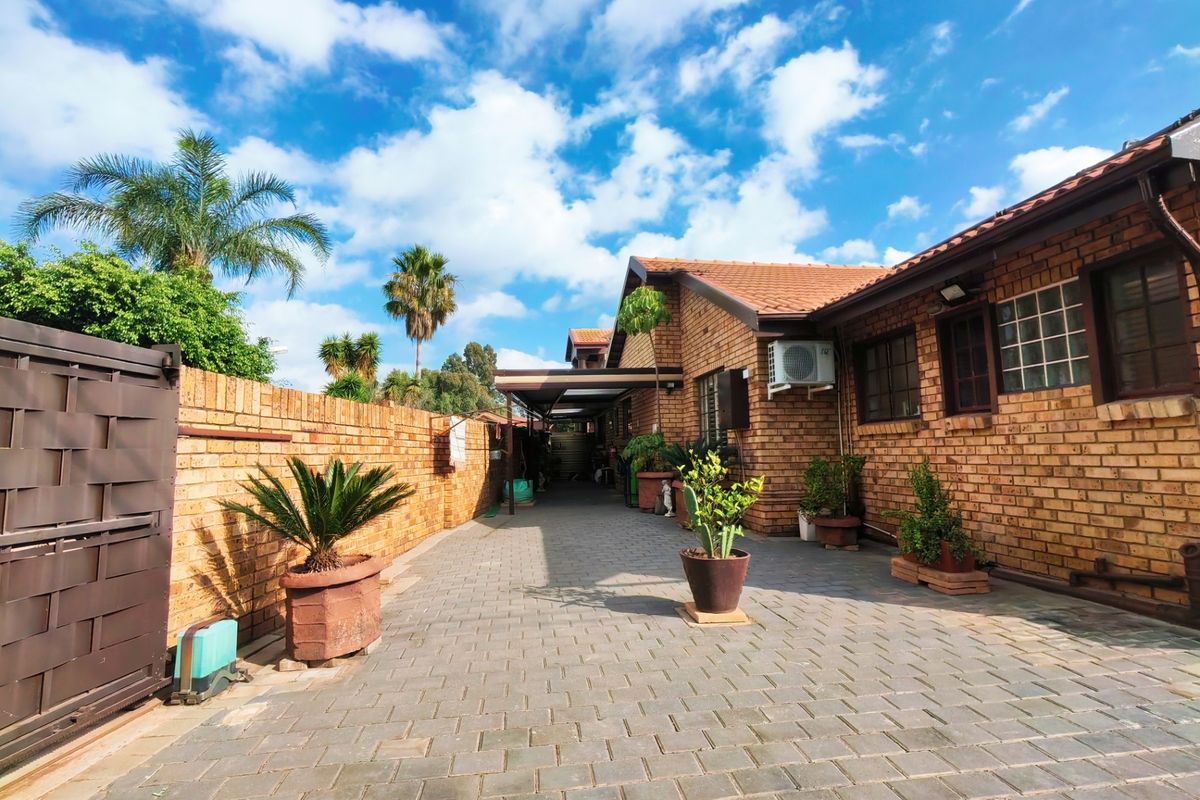 A well-maintained rear exterior area featuring face brick walls, a paved driveway, a sliding gate, and a covered carport structure.