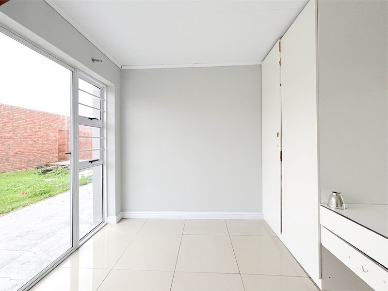 A bright, empty bedroom featuring neutral tiled flooring, built-in cupboards, and a large sliding glass door providing direct access to the garden.