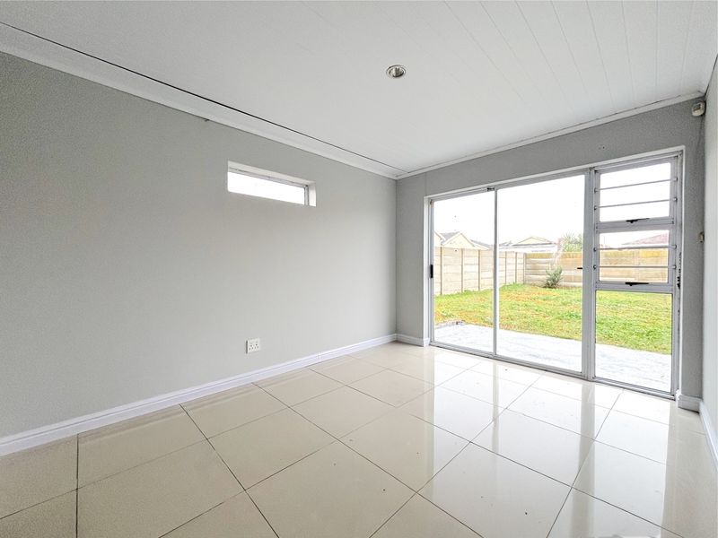 A bright, empty living room featuring neutral tiled flooring, a modern ceiling finish, and large sliding glass doors providing direct access to the rear garden.