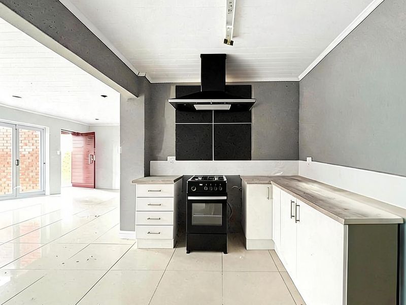 A functional kitchen area featuring white cabinetry, laminate countertops, a freestanding stove with extractor fan, and neutral tiled flooring in an open-plan layout.
