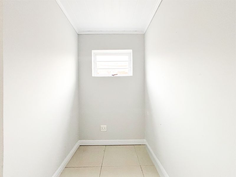 A clean, empty utility space featuring neutral tiled flooring, a louvered window for ventilation, and a finished tongue and groove ceiling.