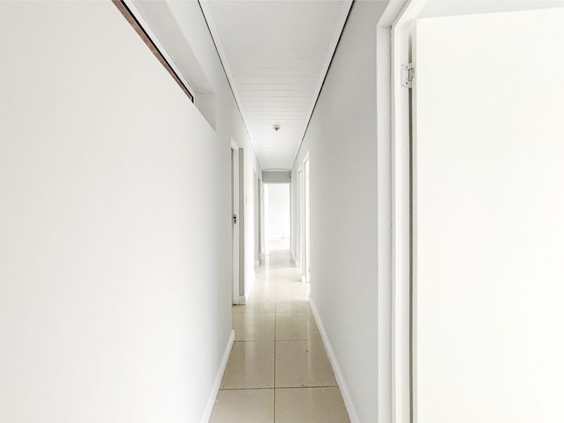 A bright, neutral hallway featuring tiled flooring and a clean, minimalist aesthetic, providing access to multiple rooms throughout the property.