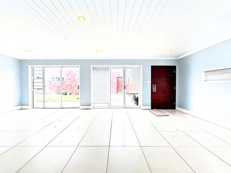 A bright, spacious, and empty living area featuring large sliding glass doors, tiled flooring, and a modern tongue and groove ceiling with recessed lighting.