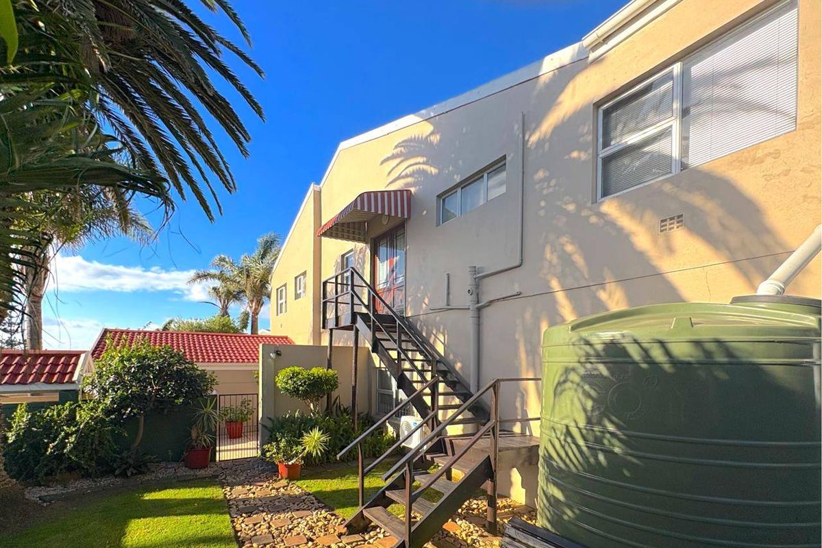 Rear exterior view of the property featuring a metal staircase, water storage tank, and landscaped garden area.
