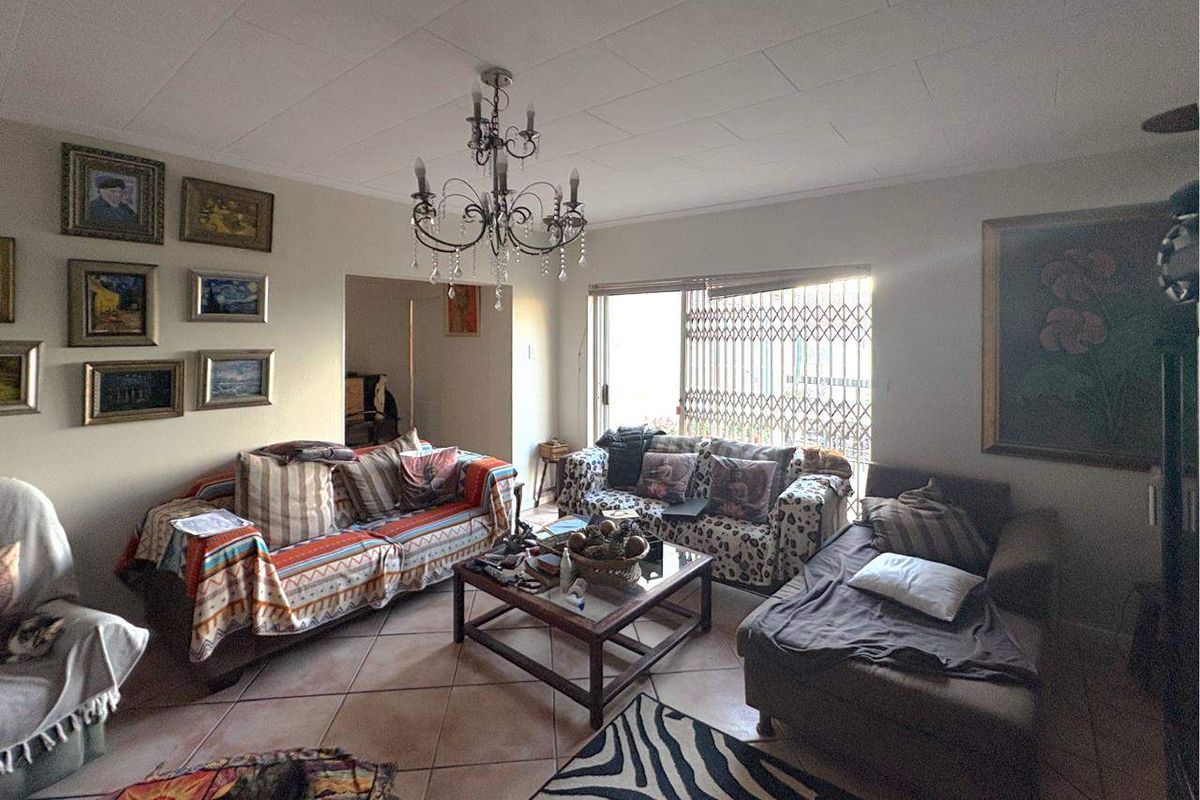 A spacious living room featuring tiled flooring, a decorative chandelier, and sliding glass doors with security gates leading to an outdoor area.