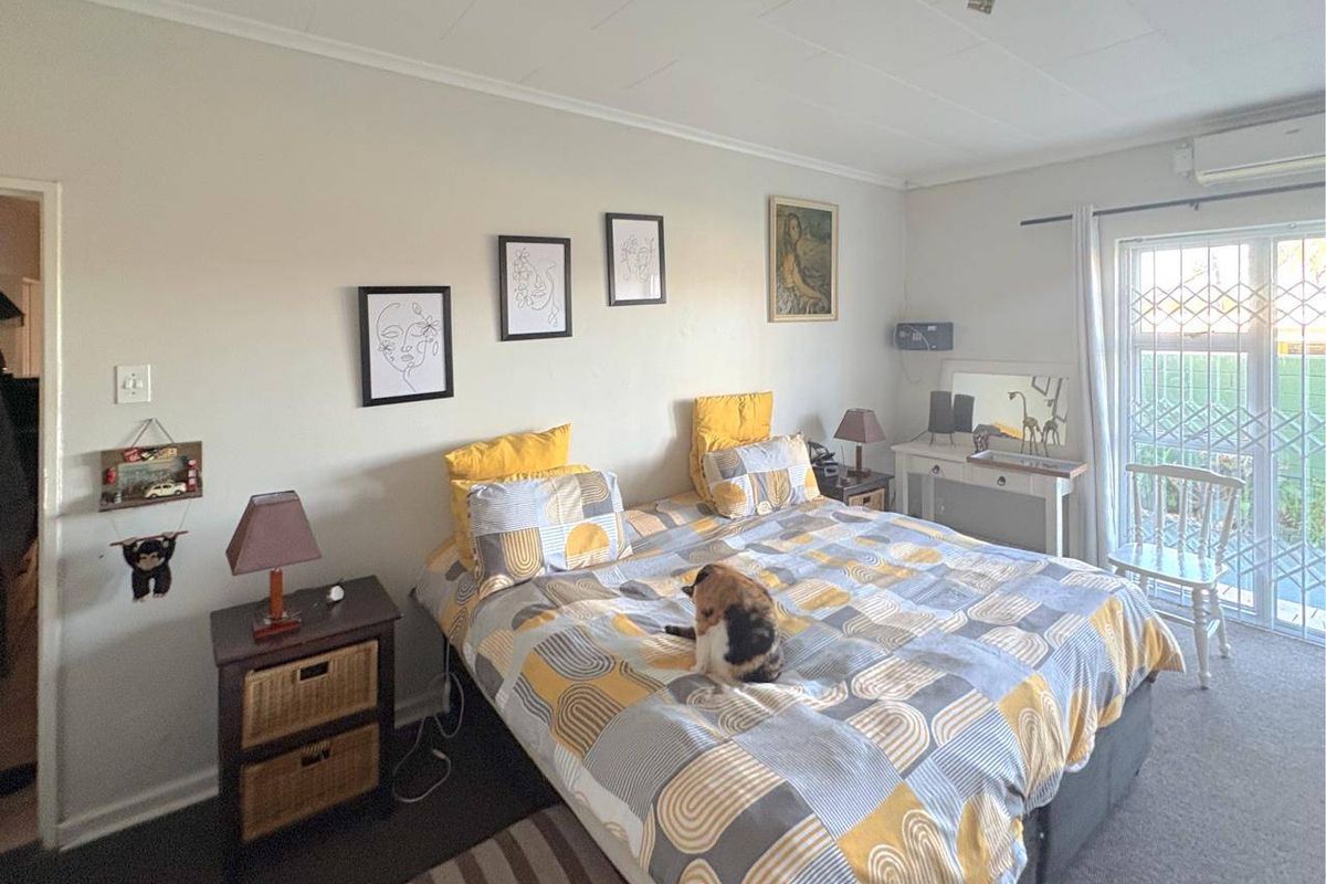 A well-lit bedroom featuring a split-system air conditioning unit and a sliding glass door with security gate leading to the exterior.