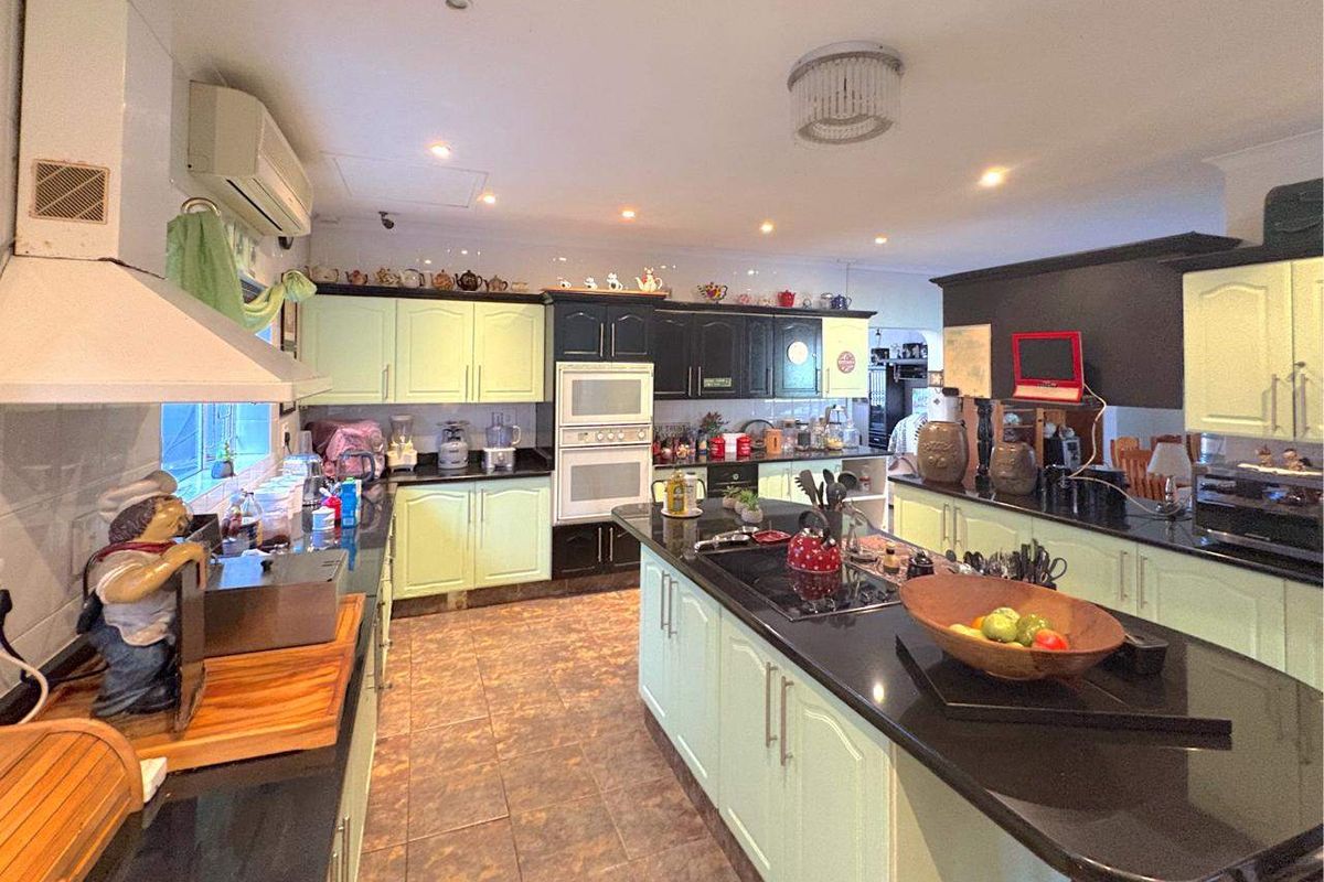 Spacious kitchen featuring a large central island, built-in double oven, integrated cooktop, and ample cabinetry with contrasting light green and black finishes.