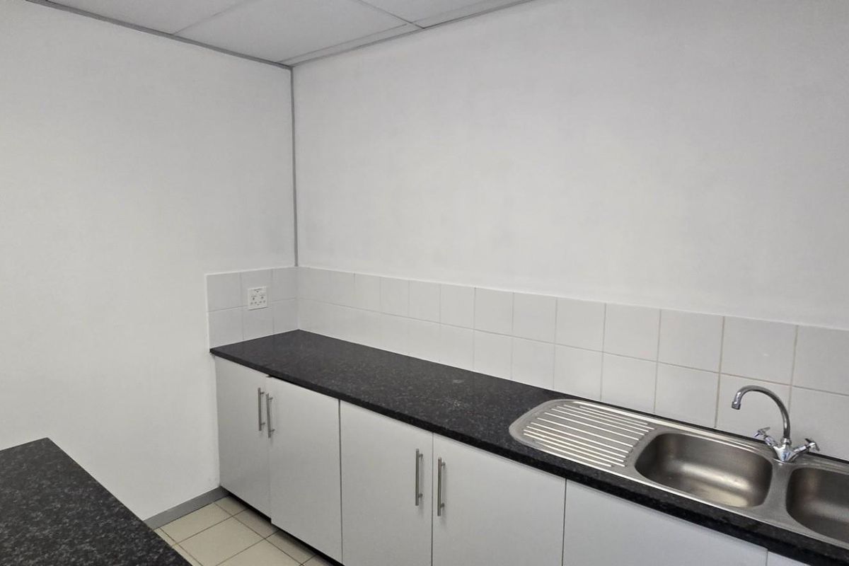 A functional commercial kitchenette featuring white cabinetry, dark granite-look countertops, a stainless steel double sink, and tiled splashbacks.