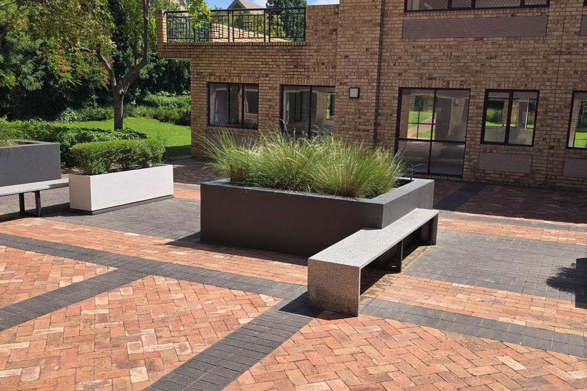A well-maintained paved courtyard area featuring built-in stone benches and integrated planter boxes, adjacent to a brick commercial building facade.