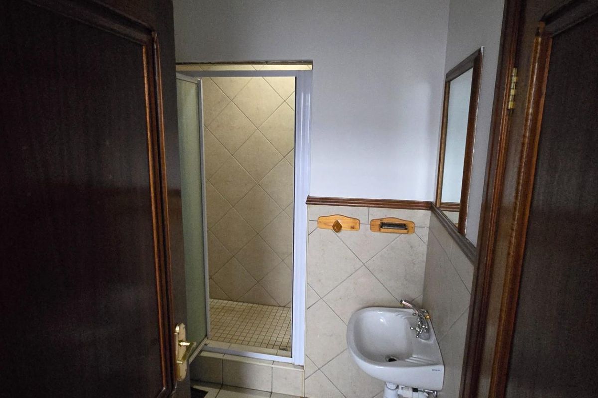 A compact bathroom featuring a pedestal sink, wall-mounted mirror, and a separate shower enclosure with tiled walls.