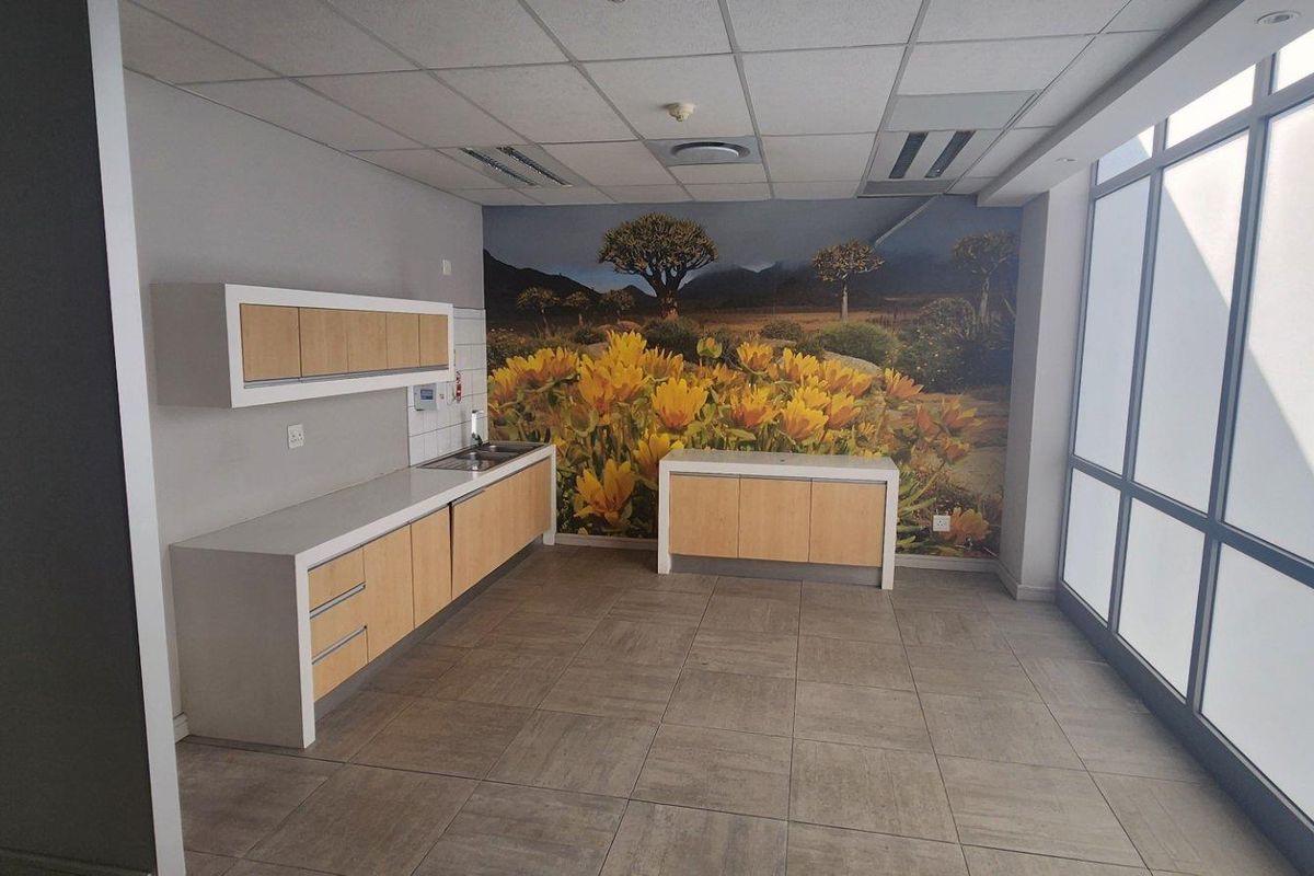 A modern commercial kitchenette featuring light wood cabinetry, white countertops, a stainless steel sink, and a large decorative wall mural.