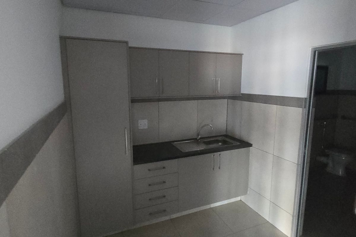 A compact kitchenette featuring modern grey cabinetry, a dark countertop, and a stainless steel sink, with tiled walls and flooring.