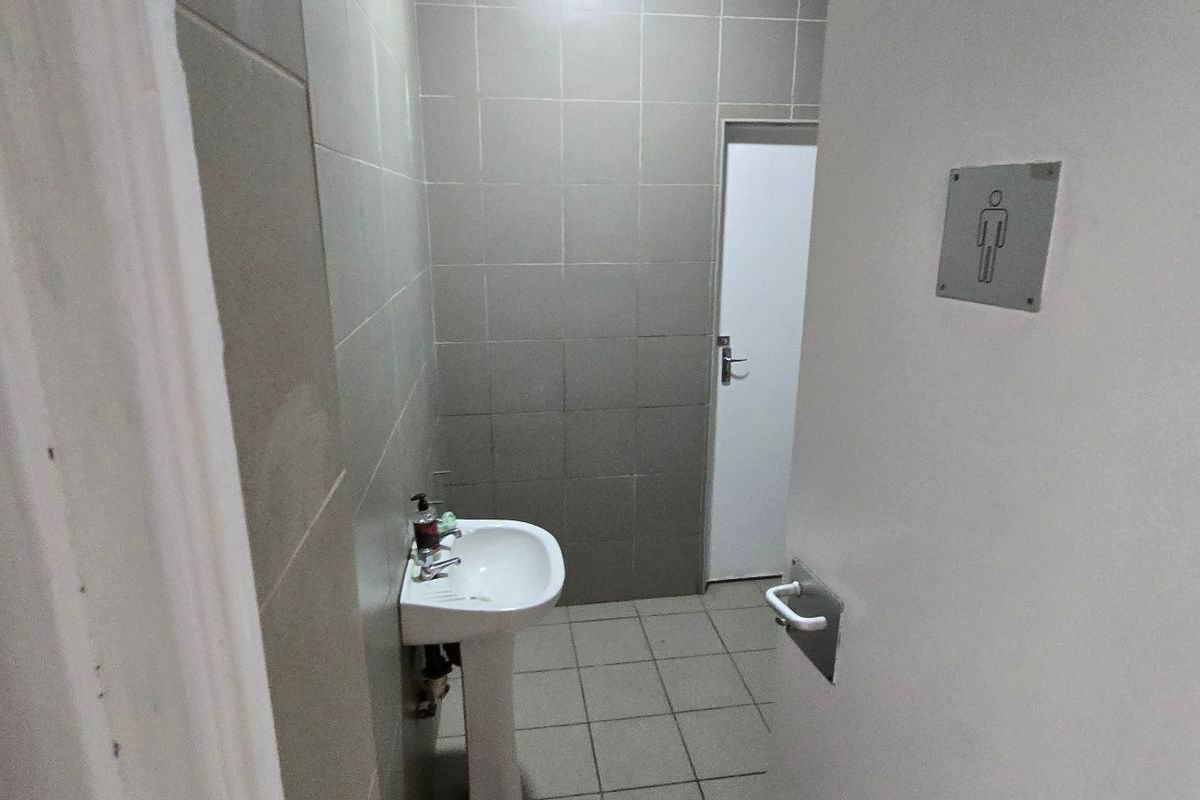 A functional industrial-style restroom featuring a pedestal basin, tiled walls, and tiled flooring, maintained in a clean and simple condition.