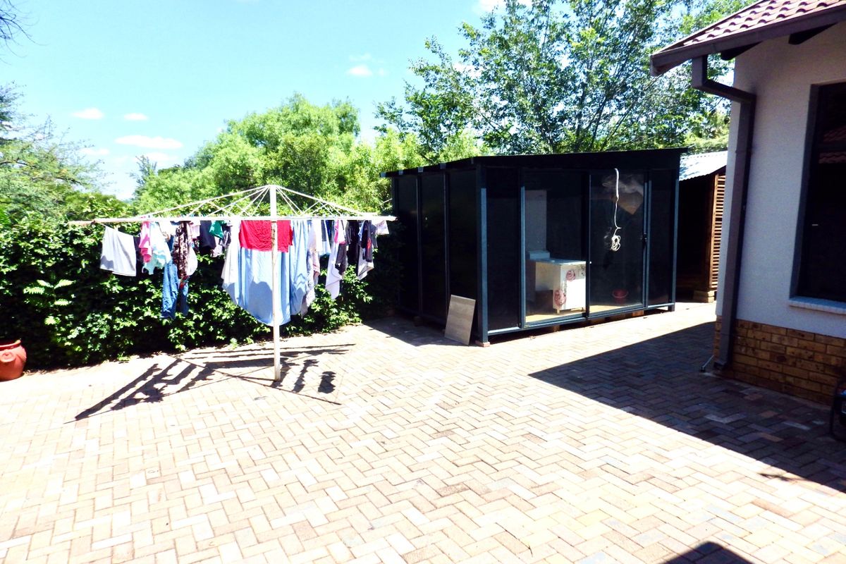Rear exterior area featuring paved patio, established garden hedge, and a detached modern utility structure.