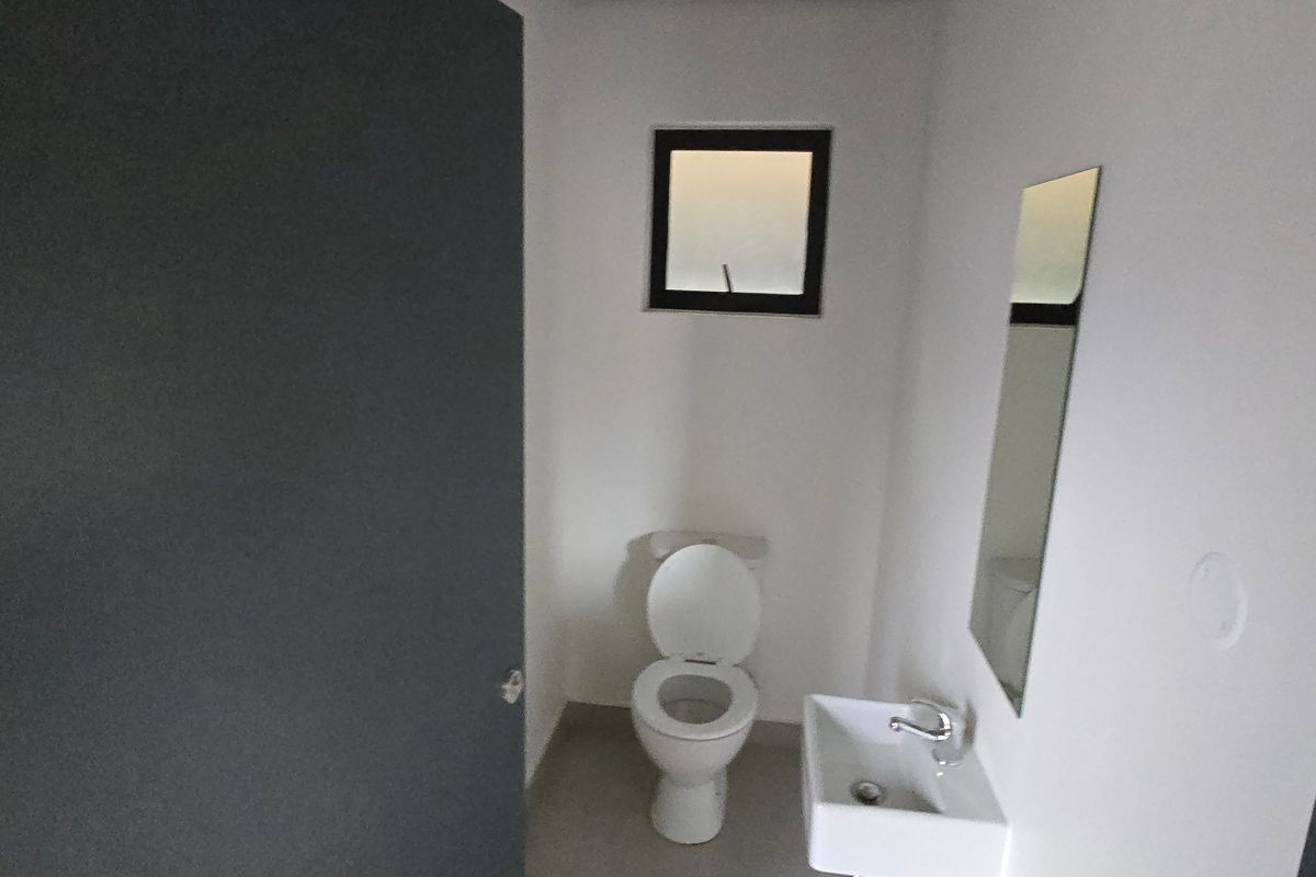 A compact industrial-style powder room featuring a wall-mounted basin, a standard toilet, and a small window for ventilation.