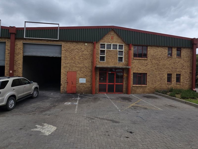 Front elevation of an industrial warehouse unit featuring face brick construction, roller shutter doors, and a paved forecourt area.