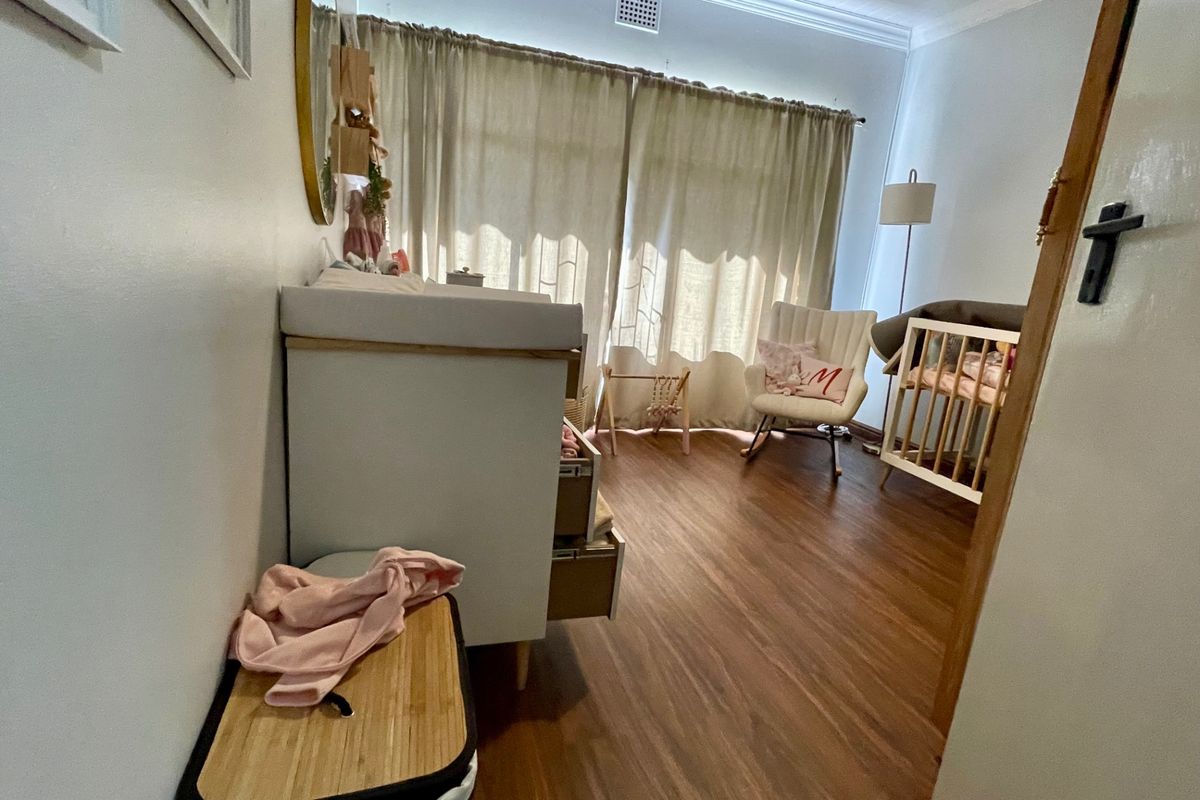 A well-maintained bedroom featuring wood-look flooring, crown molding, and large windows with floor-to-ceiling curtains, providing a bright and comfortable living space.