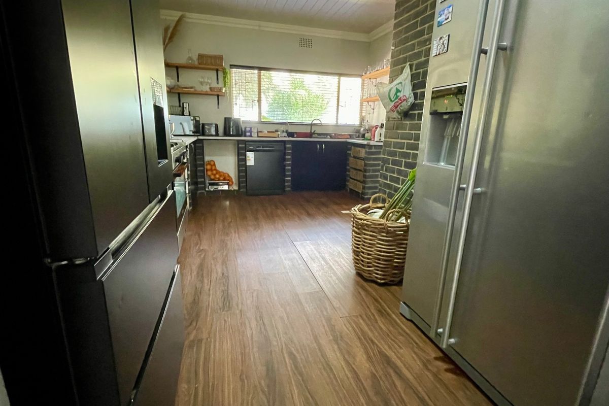 A functional kitchen featuring wood-look flooring, brick accent walls, open shelving, and integrated appliance spaces with a view of the garden.
