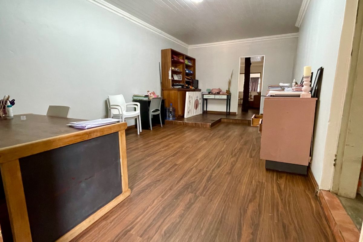 A multi-purpose living space featuring wood-look laminate flooring, crown molding, and a raised platform area leading to an adjacent room.