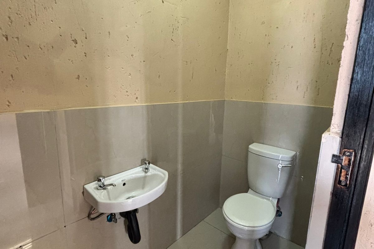 A compact industrial-style bathroom featuring a wall-mounted basin and a standard toilet with tiled flooring and partially tiled walls.