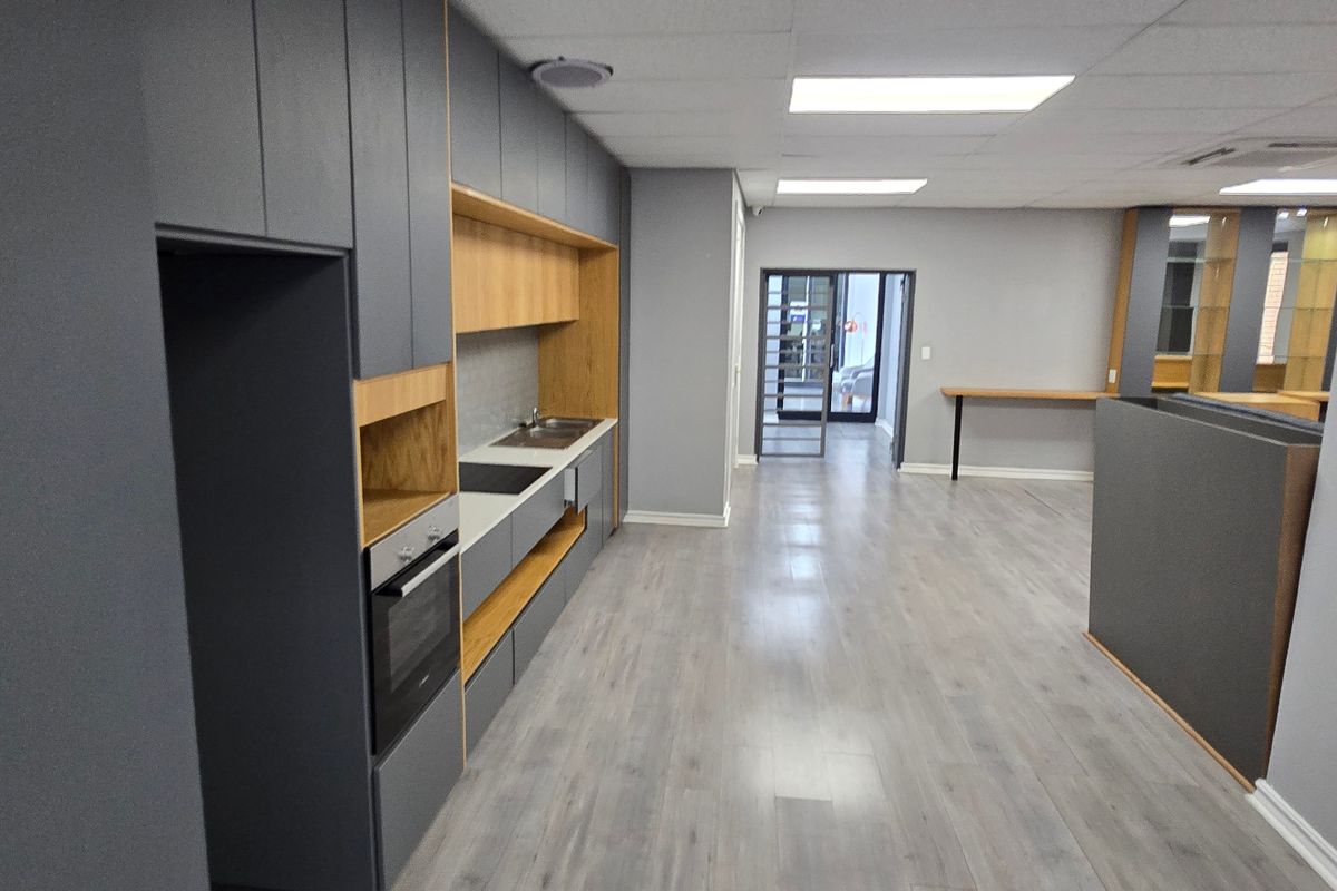 Modern commercial kitchenette featuring sleek grey cabinetry, wood-tone accents, integrated oven, and durable laminate flooring in an open-plan office environment.