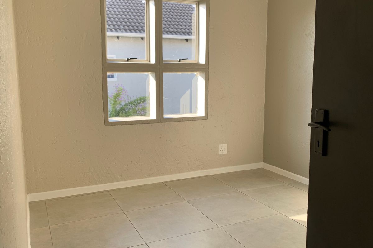 A clean, empty bedroom featuring neutral wall tones, tiled flooring, and a window providing natural light.