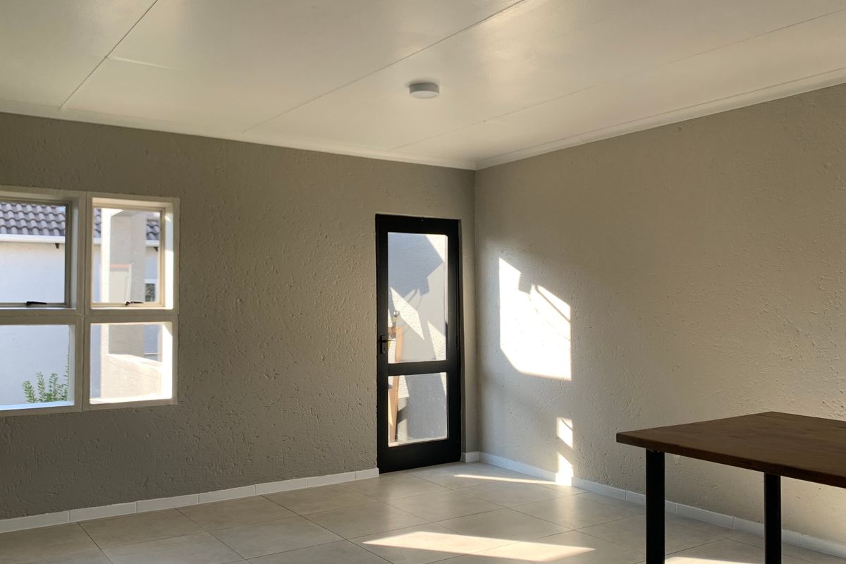 A bright, empty living area featuring neutral textured walls, tiled flooring, and a glass panel door leading to the exterior.