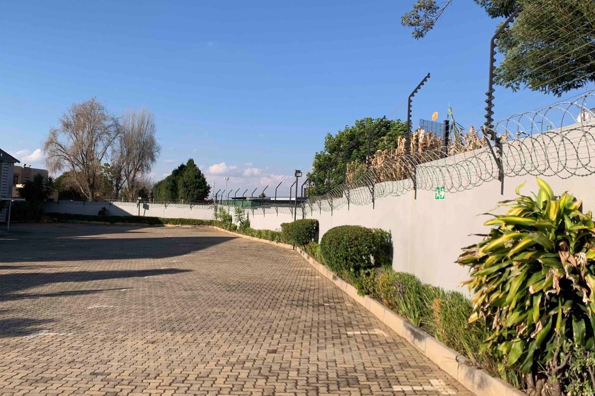A paved outdoor parking area featuring perimeter walling with security fencing and established garden borders.