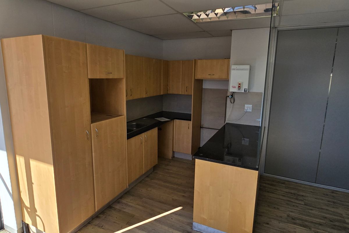 A functional kitchenette featuring light wood cabinetry, dark countertops, a stainless steel sink, and a wall-mounted electric water heater.