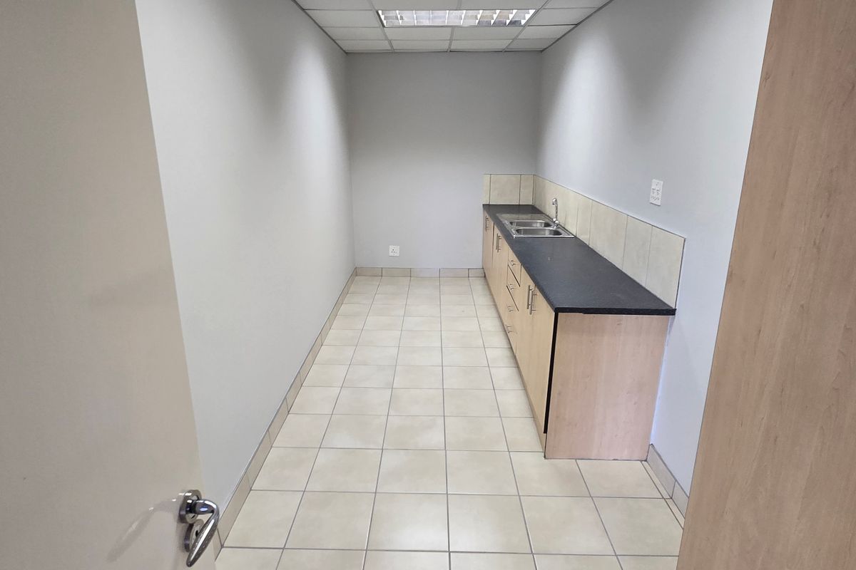 A functional kitchenette area featuring built-in cabinetry, a countertop with a sink, tiled flooring, and a drop ceiling with integrated lighting.